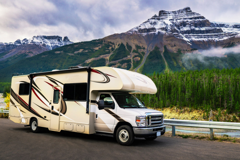 When you buy a used RV, you can enjoy the RV life at a lower price point. This Class C RV is parked in front of snow capped mountains.