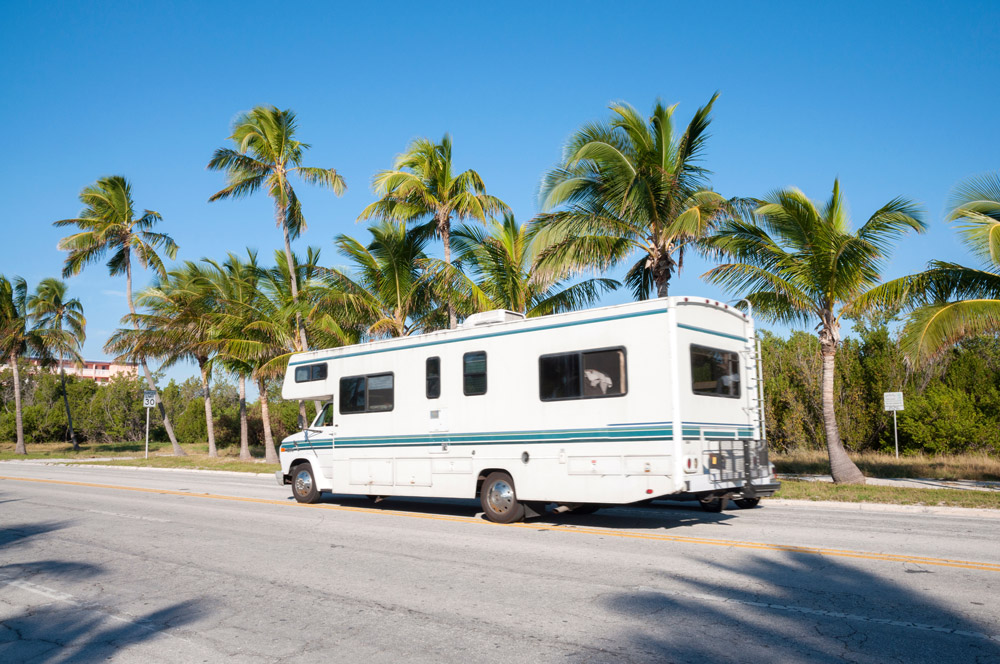 An RV drives past palm trees in Florida.
